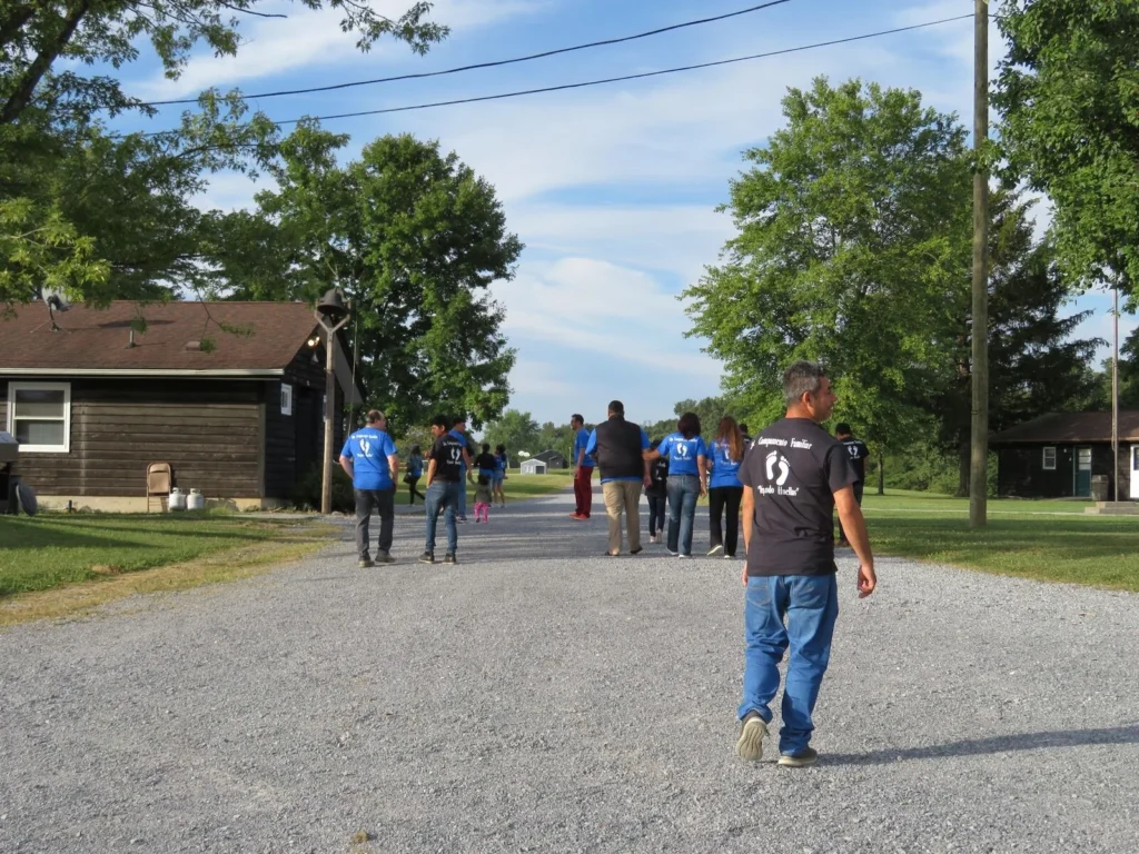 Familias caminan por un camino de grava entre cabañas y árboles en el campamento familiar
