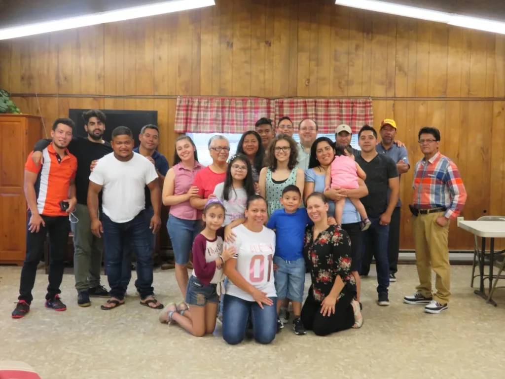 La congregación posa para una foto de grupo en un salón con paredes de madera