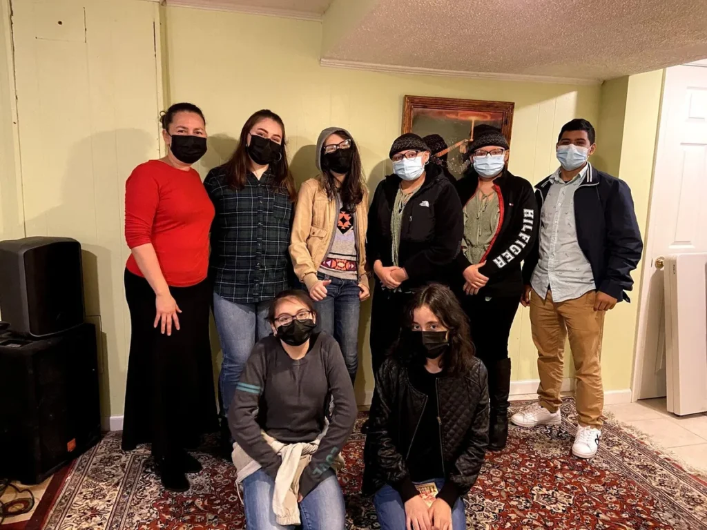Grupo de jóvenes con mascarillas posa junto a una líder en un salón